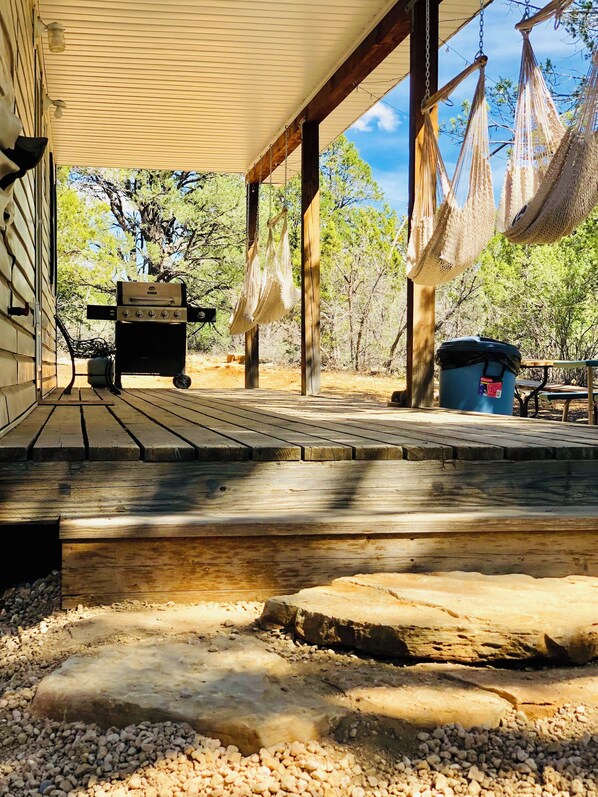 A covered outdoor area with a grill, hammocks, and a trash can.