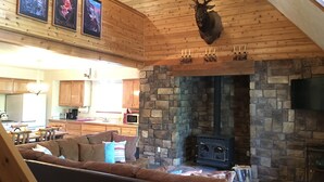 A cozy cabin interior with a stone fireplace, wooden ceiling, and a mounted elk head.