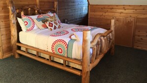 A wooden four-poster bed with a patterned bedspread and pillows, set in a room with wooden walls and a sloped ceiling.