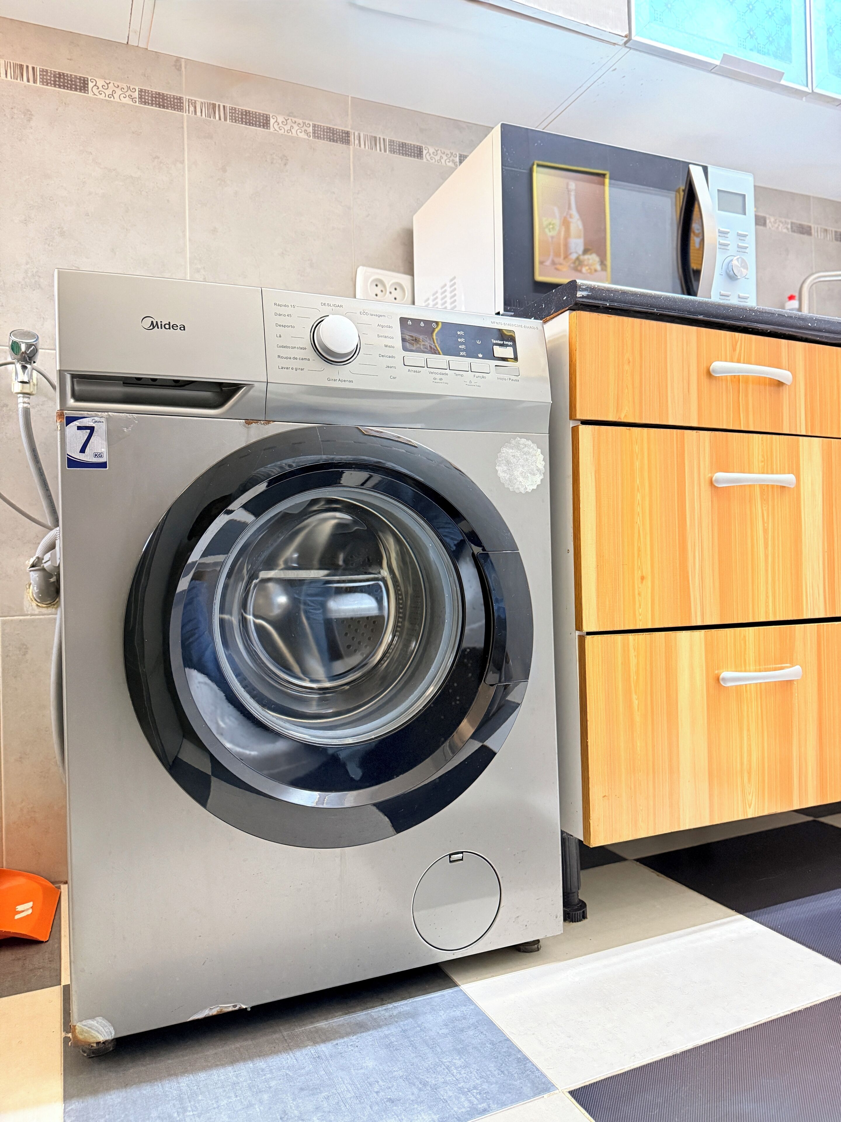 A front-loading washing machine with a control panel, a wooden cabinet with drawers, and a tiled floor.
