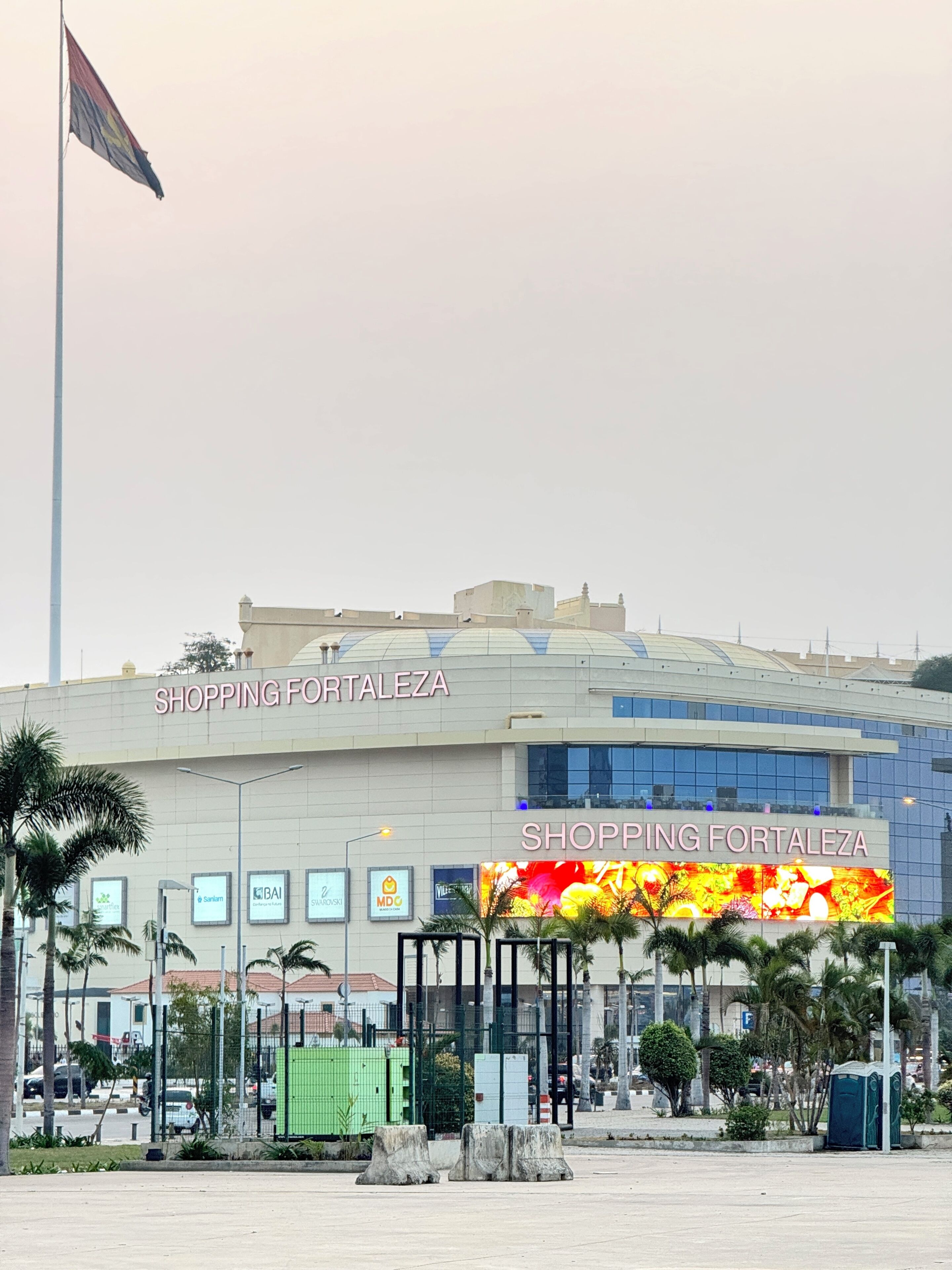 A shopping mall named Shopping Fortalezaza with a large sign, palm trees, and a flag.