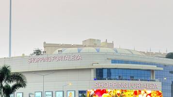 A shopping mall named Shopping Fortalezaza with a large sign, palm trees, and a flag.