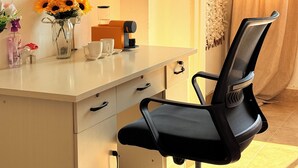 Ein moderner Arbeitsraum mit einem weißen Schreibtisch, einem schwarzen Bürostuhl, einer Kaffeemaschine und einer Vase mit Sonnenblumen.