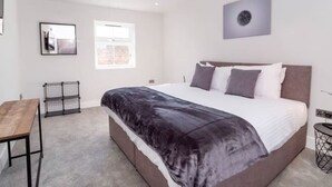 A modern bedroom with a large bed, a desk, and a window.