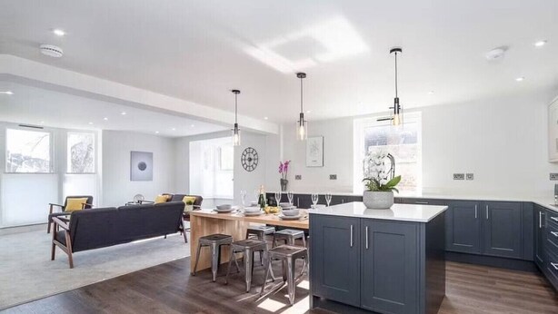 A spacious kitchen with a central island, dark wooden flooring, and modern pendant lighting.