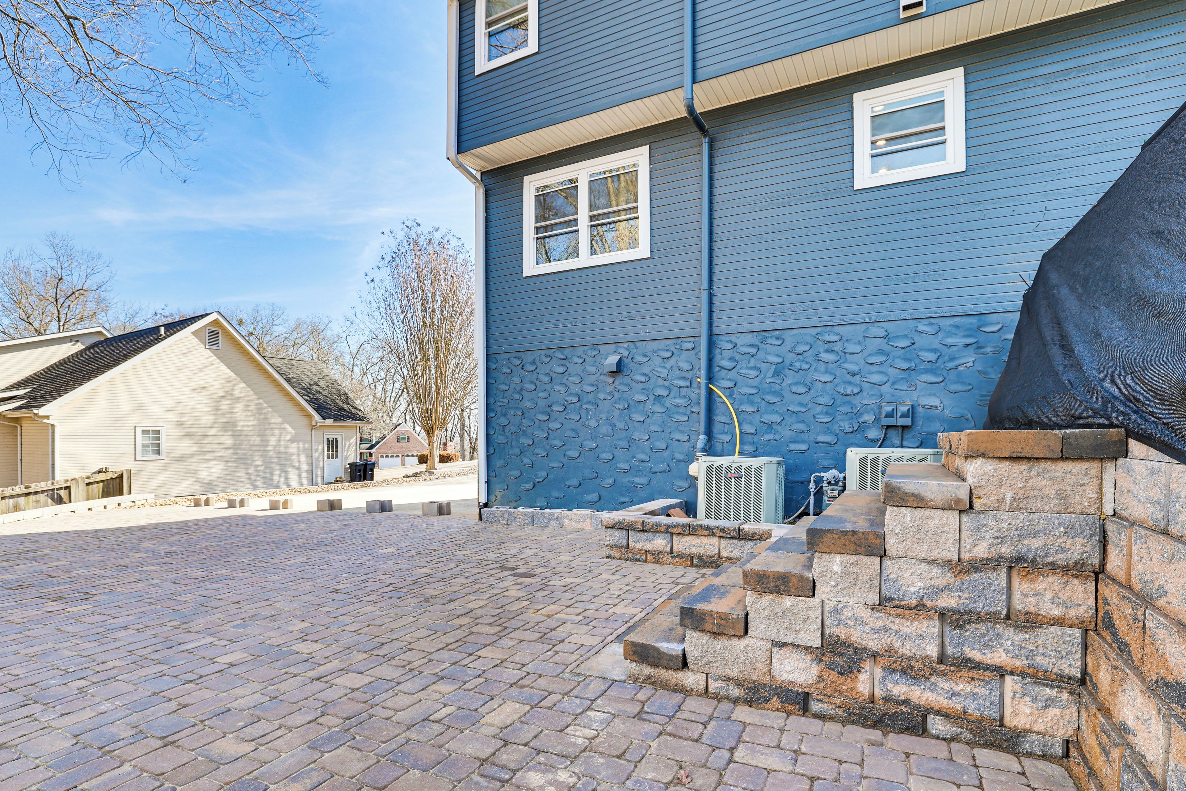 Un immeuble résidentiel à la façade bleue, avec une allée pavée en briques et un escalier en pierre menant à une zone abritée.