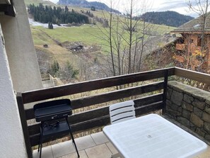 A balcony with a grill, a table, and a stone wall. - View mountain, terrace, tv, ski locker, 18m², Le Grand Bornand (Le Grand-Bornand)