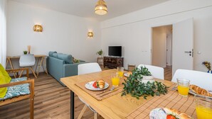 A modern living room with a sofa, dining table, and TV. - #281 Telecomunicações by Home Holidays (Albufeira)