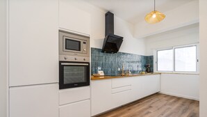 A modern kitchen with white cabinetry, a built-in oven, a microwave, and a black range hood. - #281 Telecomunicações by Home Holidays (Albufeira)