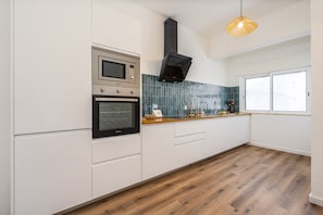A modern kitchen with white cabinetry, a built-in oven, a microwave, and a black range hood. - #281 Telecomunicações by Home Holidays (Albufeira)
