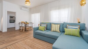 A living room with a sofa, a dining table with chairs, and a kitchen area with an oven. - #281 Telecomunicações by Home Holidays (Albufeira)