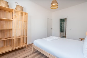 A bedroom with a wooden wardrobe, a bed with white linens, and a hanging light fixture.