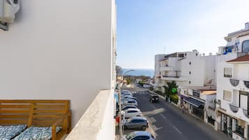 A balcony with a wooden bench, a row of parked cars, and buildings along a street.