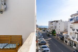 A balcony with a wooden bench, a row of parked cars, and buildings along a street. - #281 Telecomunicações by Home Holidays (Albufeira)
