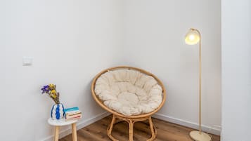 A corner room with a round, cushioned chair, a small table with a vase and books, and a floor lamp.