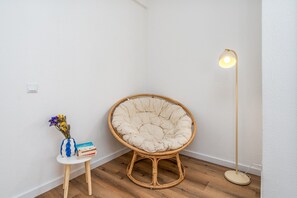 A corner room with a round, cushioned chair, a small table with a vase and books, and a floor lamp.