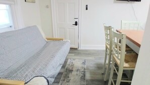 Quarto com cama, mesa de jantar com cadeiras, televisão fixada na parede e uma porta.