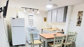 Uma cozinha compacta com geladeira, micro-ondas e fogão. Há uma mesa de jantar com cadeiras e um pequeno tapete no chão.