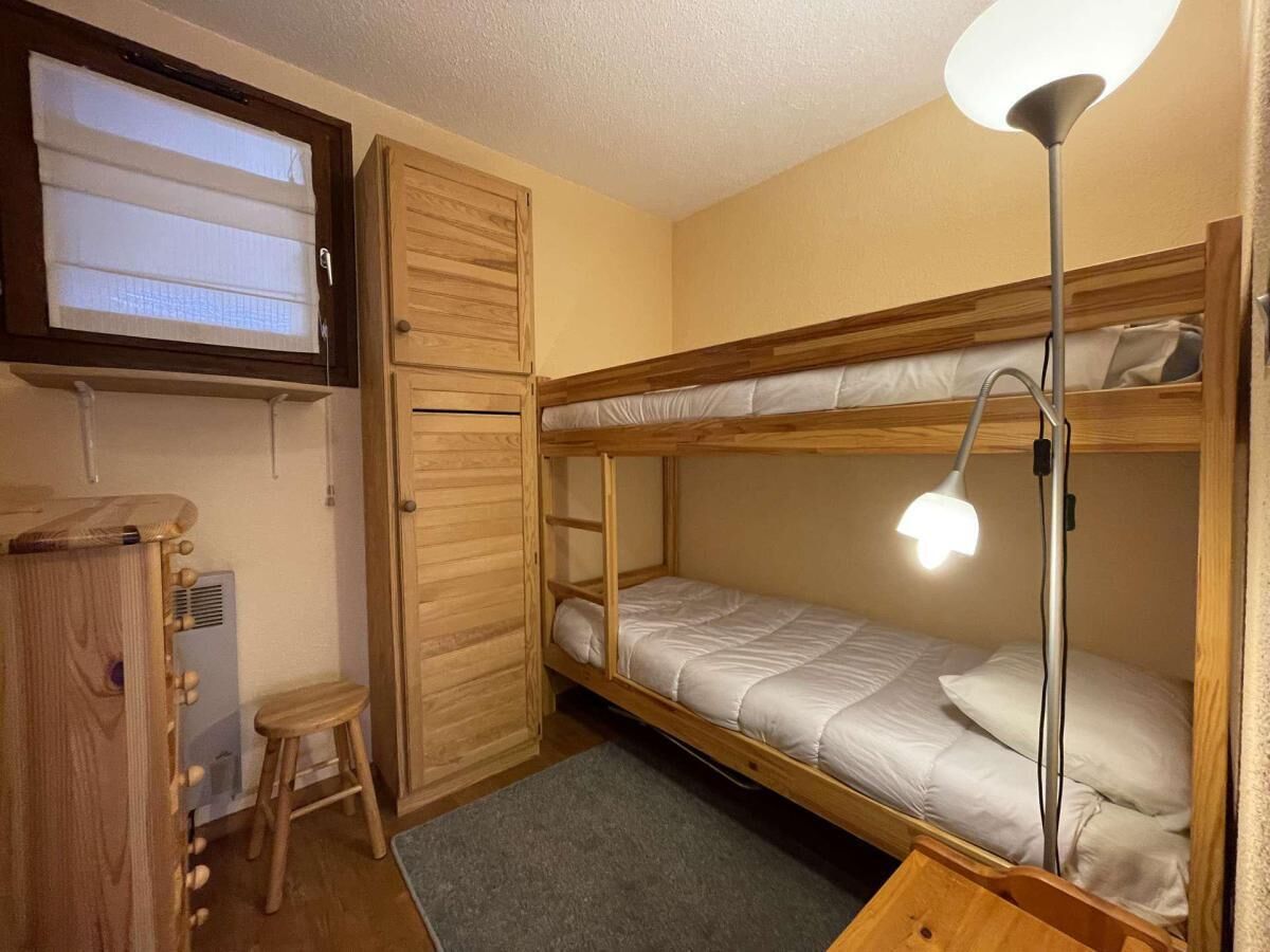 Une petite pièce comprenant un lit superposé, un bureau avec une chaise, une lampe sur pied et une armoire.