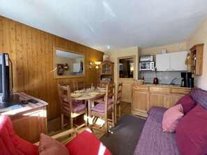 A cozy cabin-style room with a dining table, chairs, a sofa, and a kitchenette.