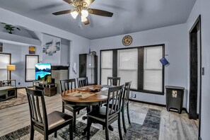 A modern living room with a round wooden table, dark chairs, a ceiling fan, a TV, and a large window with blinds. - Family-Friendly 6-bedroom house in Charming Buffalo with WiFi, AC (Buffalo)