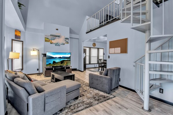 A modern living room with a flat-screen TV, grey sofas, a dining area, and a staircase. - Family-Friendly 6-bedroom house in Charming Buffalo with WiFi, AC (Buffalo)