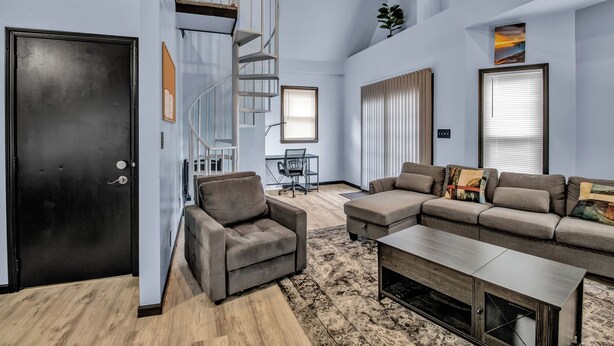 A modern living room with a curved staircase, a sofa set, a coffee table, and a desk with a chair. - Family-Friendly 6-bedroom house in Charming Buffalo with WiFi, AC (Buffalo)