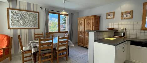 Une cuisine moderne avec des meubles en bois, un coin repas comprenant une table et des chaises, et une vue sur l’extérieur par une fenêtre.