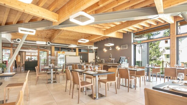 Tilava ravintola, jossa on puupalkit, modernit riippuvalaisimet ja näkymä ulos.
