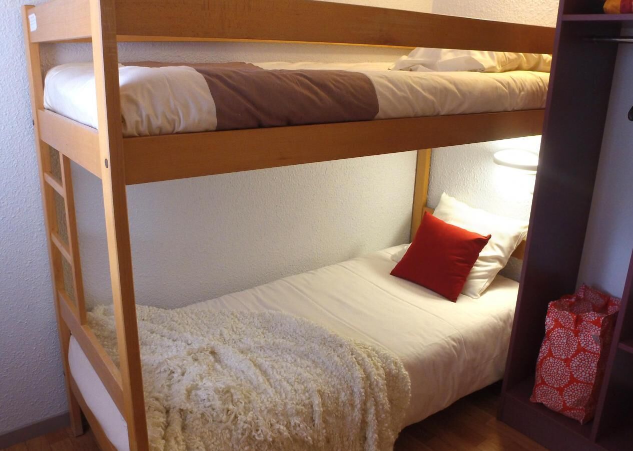 Une chambre avec un lit superposé, le lit du bas étant équipé d’un oreiller rouge et d’une couverture blanche.
