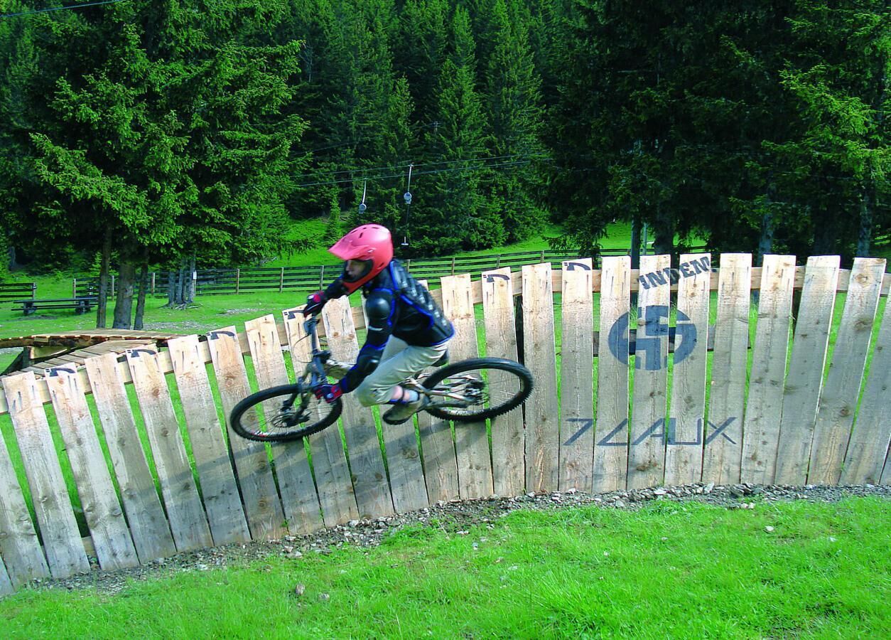 Eine Person fährt mit einem Mountainbike über eine Holzbarriere.