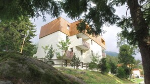 A two-story building with a white facade and wooden accents, surrounded by trees and a rocky hill. - 10m from ski slopes, tv, ski locker, 60m², Les 7 Laux (Les Adrets)