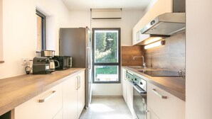 Eine moderne Küche mit integriertem Backofen, einer Kaffeemaschine und einem Fenster mit Blick auf Grünflächen.