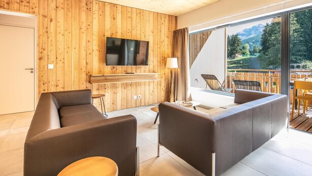 Ein modernes Wohnzimmer mit einer Holzvertäfelung, einem Flachbildfernseher, einem Sofa, einem Couchtisch und einem Balkon mit Gartenmöbeln.