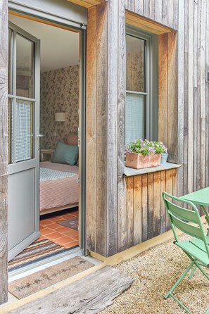 A wooden exterior with a sliding door leading to a bedroom with floral wallpaper and a bed. - à la Mainguère (Brece)