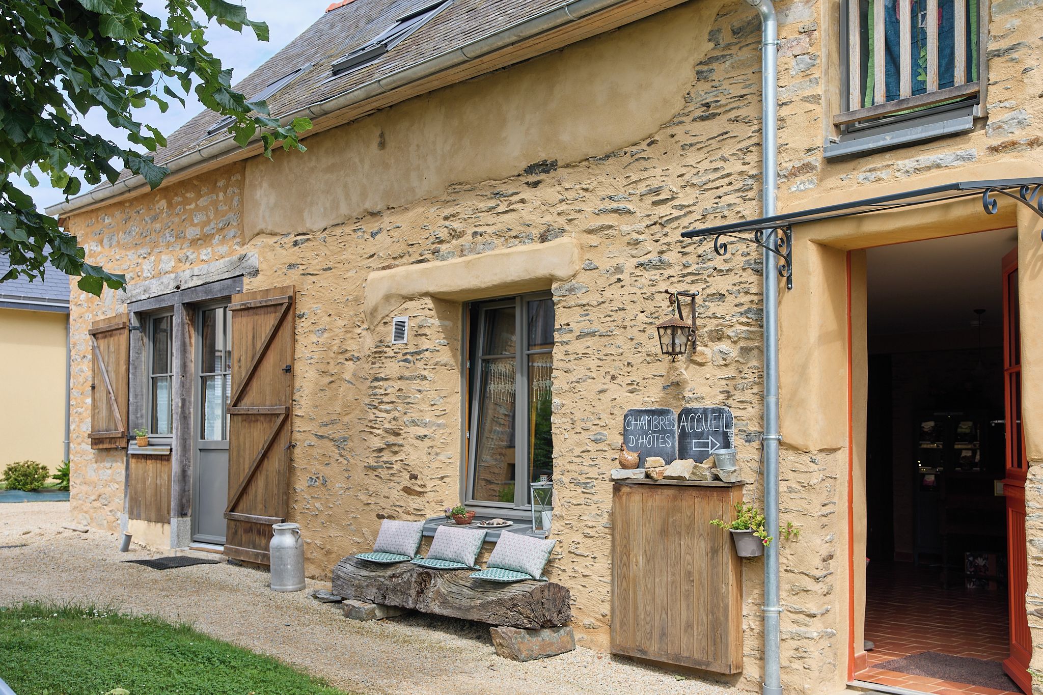 A rustic building with a stone facade, wooden shutters, and a sign indicating it's a guesthouse.