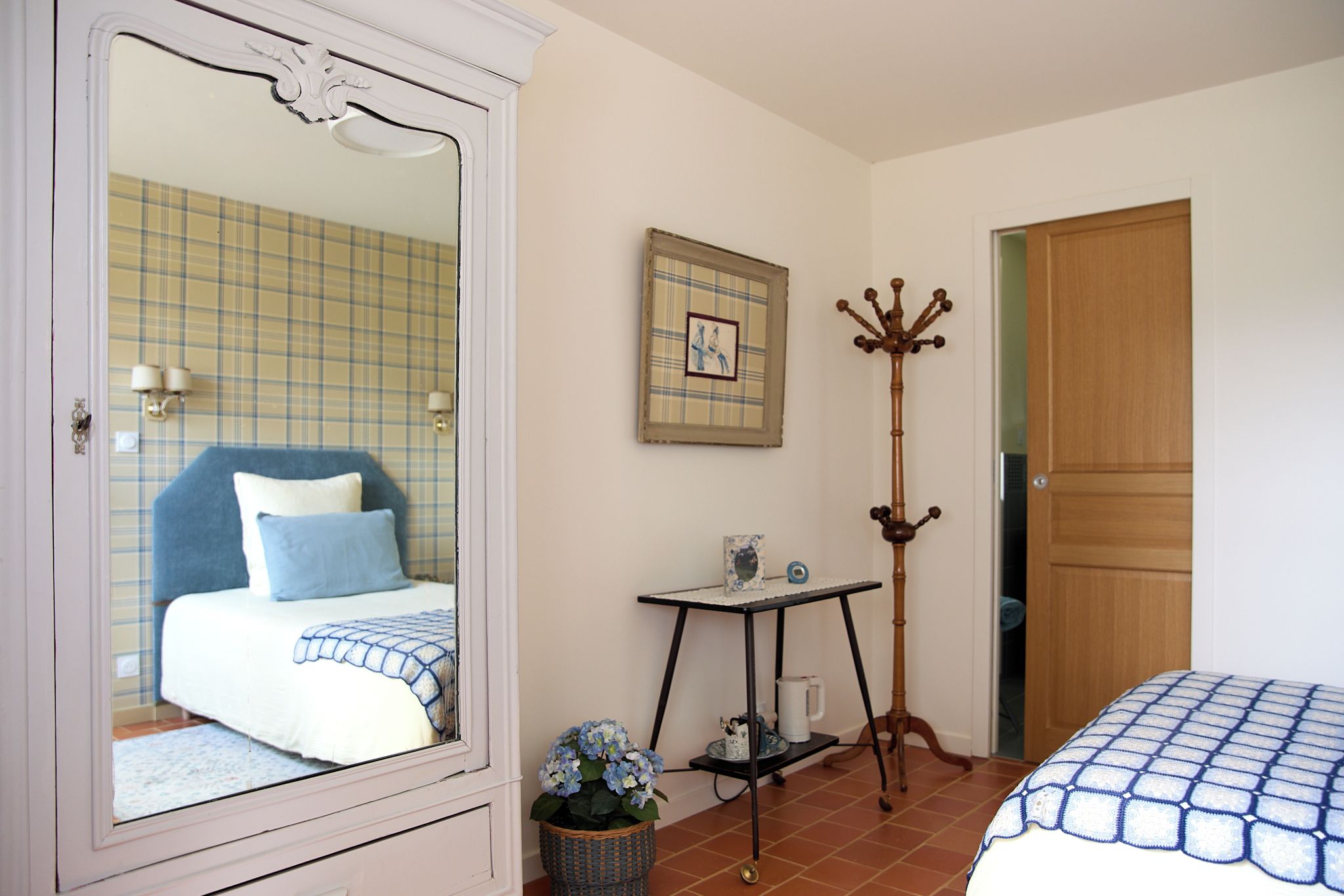 A bedroom with a bed, a dresser, a table with a vase, and a coat rack.