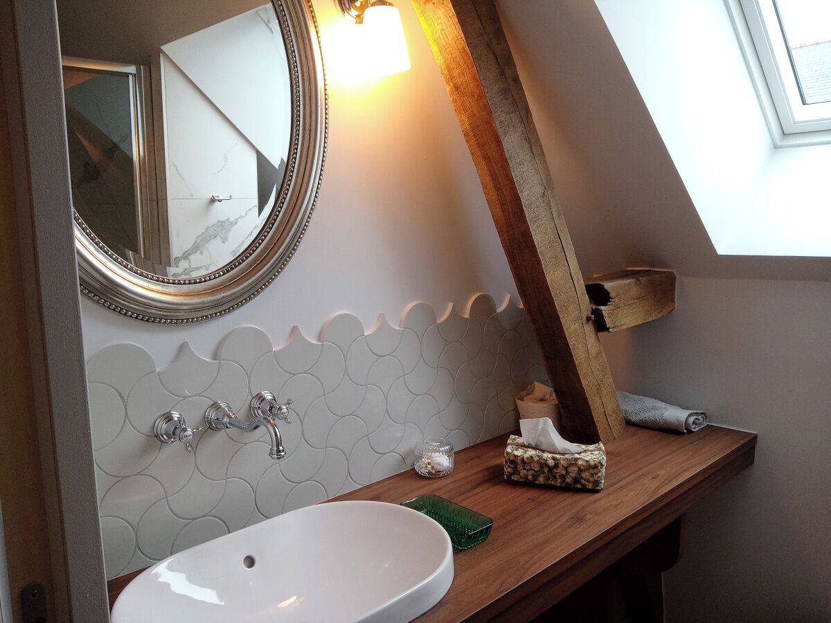 Un baño con un lavamanos blanco, un espejo y un estante de madera.