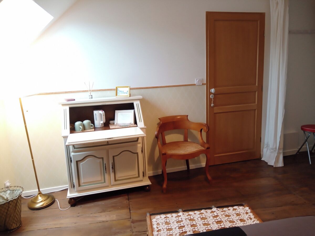 A room with a white cabinet, a wooden chair, a door, and a small table with a lace tablecloth.
