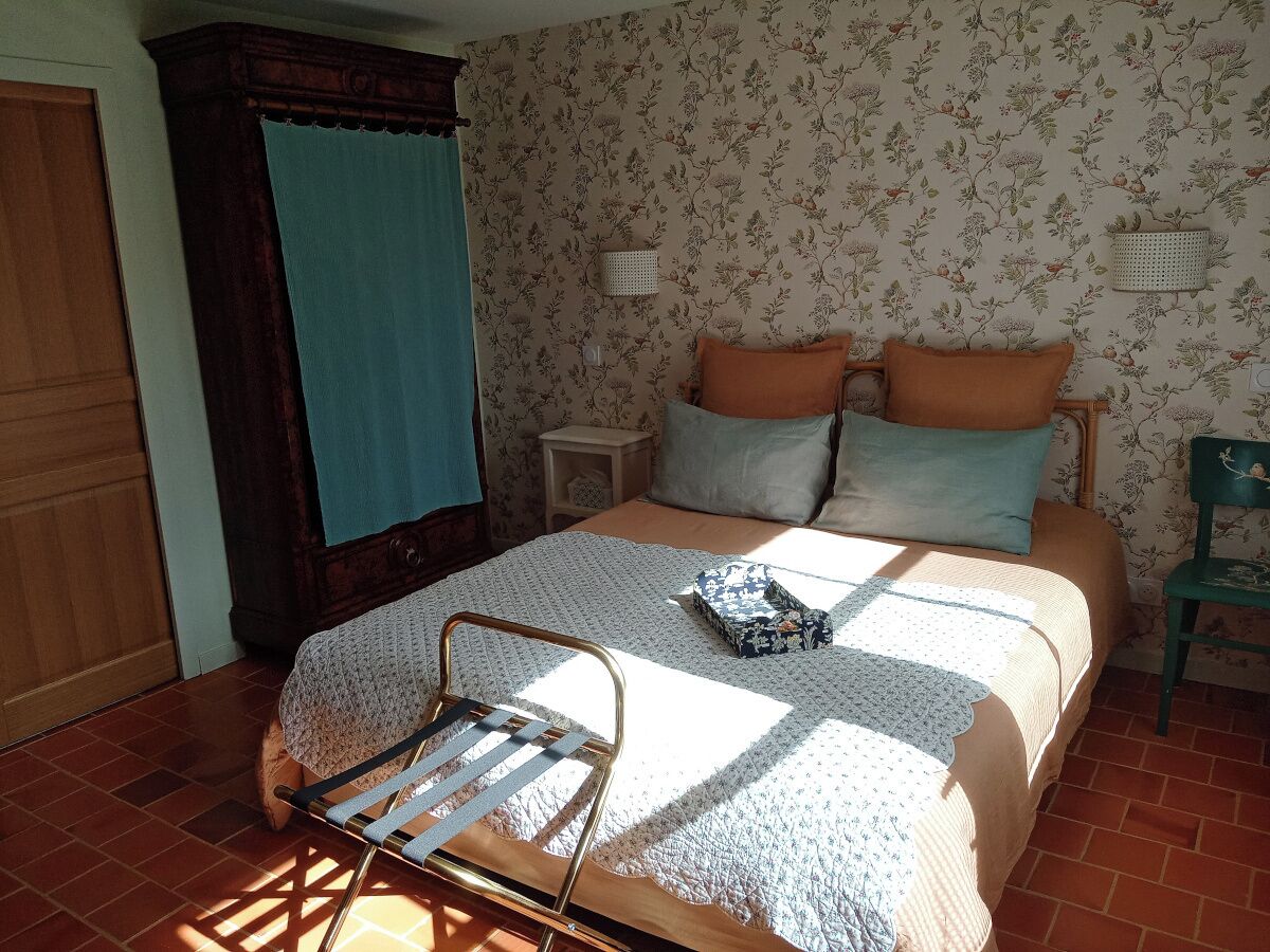 Un dormitorio con cama, mesita de noche, una silla y una ventana con cortinas.