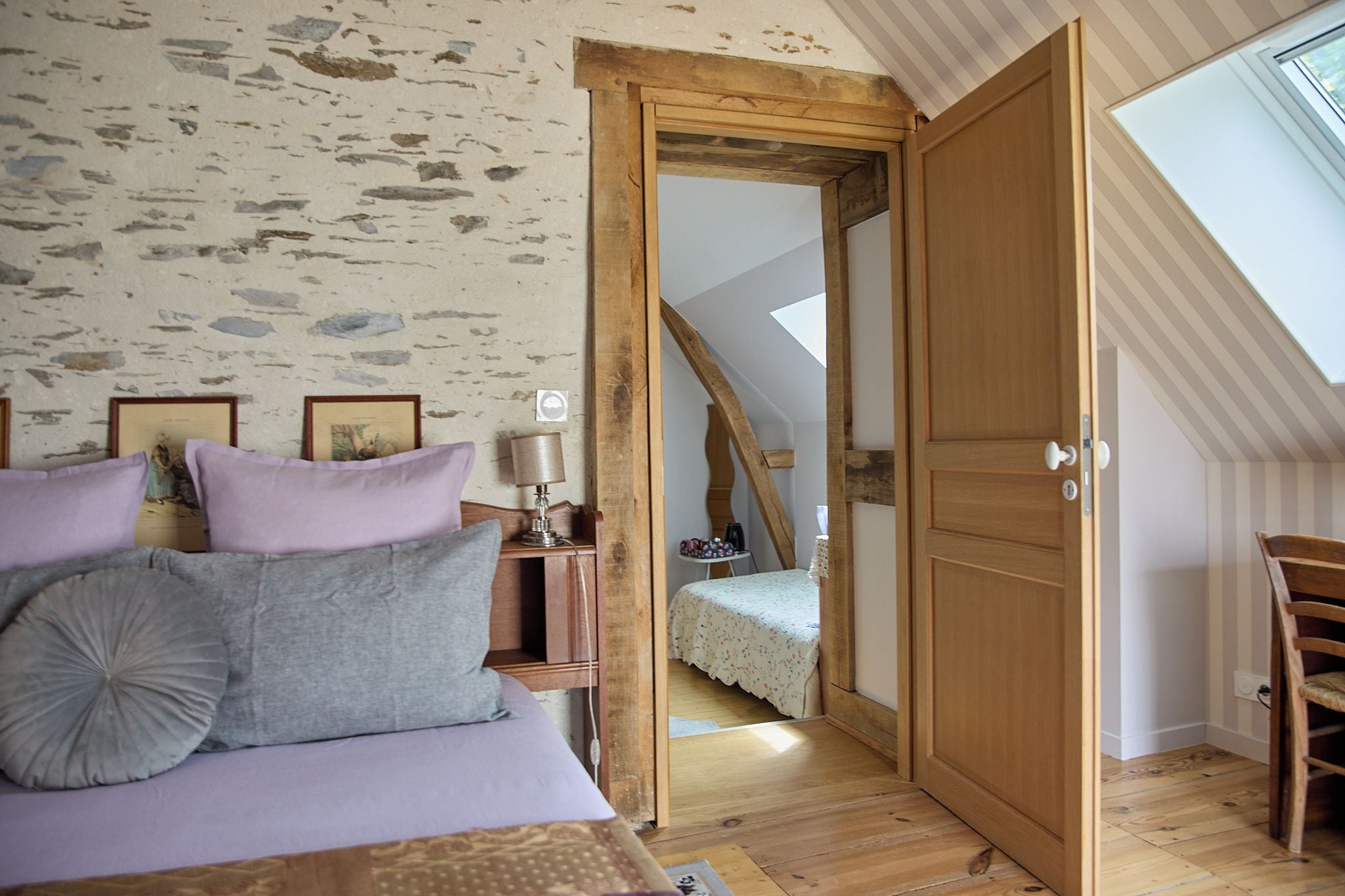 Une chambre à coucher comprenant un lit, une table de chevet, une lampe et une porte en bois donnant sur une chambre située en mezzanine.