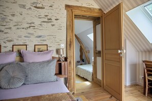 A bedroom with a bed, a nightstand, a lamp, and a wooden door leading to a loft bedroom. - à la Mainguère (Brece)