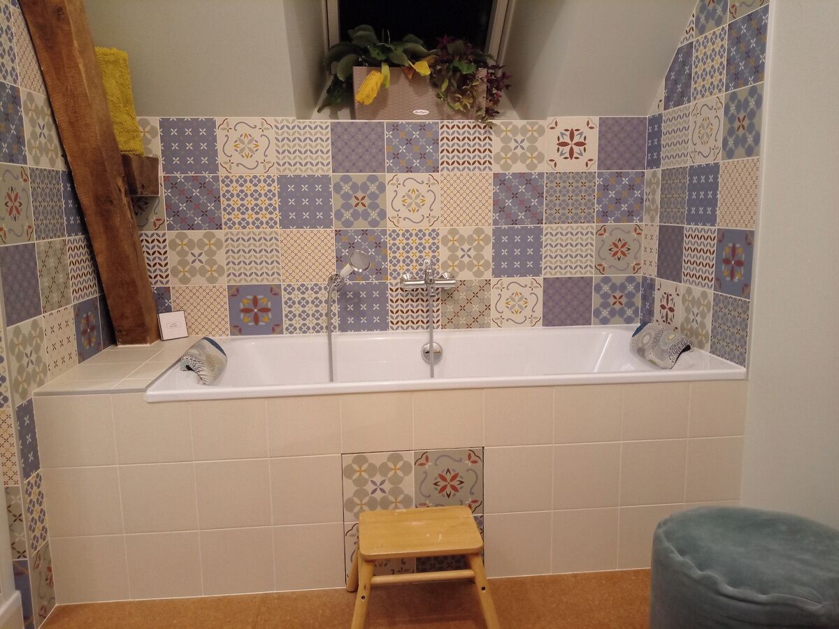 Un baño con bañera, un taburete de madera y una ventana con plantas.