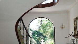 A spacious foyer with a grand staircase, a large ornate mirror, and a view of a lush garden through an arched doorway. - Villa Quebrada Estate (Cóbano)