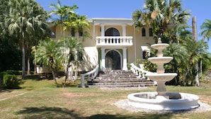 A grand entrance with a stone staircase leading to a gated door, surrounded by palm trees and a central fountain. - Villa Quebrada Estate (Cóbano)