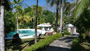 A pool area with lounge chairs, a dining setup, and a stone pathway surrounded by greenery. - Villa Quebrada Estate (Cóbano)
