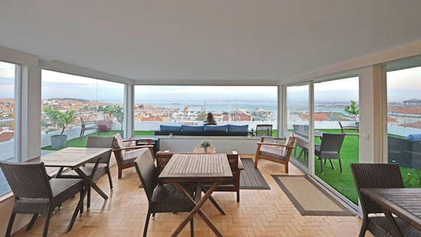 A spacious balcony with a wooden table and chairs, a sofa, and a view of the city and sea. - TheHOUSE - Your luxury home (Lisboa)