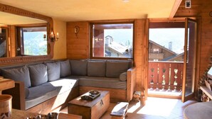 Et hyggeligt interiør i en træhytte med en stor træsofa, et lille sofabord og en balkon med gelænder af træ.