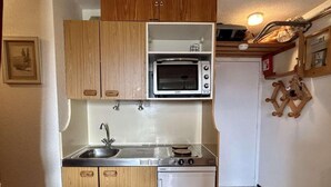 A compact kitchen with wooden cabinets, a built-in microwave, a sink, and a stove. - 100m from ski slopes, 3rd floor, tv, 27m², Alpe d'Huez (L'Alpe d'Huez)