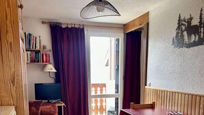 A cozy room with a wooden bed, a small desk with a lamp, a dining table with chairs, a bookshelf, and a window with curtains. - 100m from ski slopes, 3rd floor, tv, 27m², Alpe d'Huez (L'Alpe d'Huez)